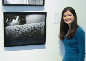 Elizabeth Moore, an NCVPS Photography student stands with her work in an exhibition in NCMA's education gallery. Courtesy North Carolina Museum of Art.